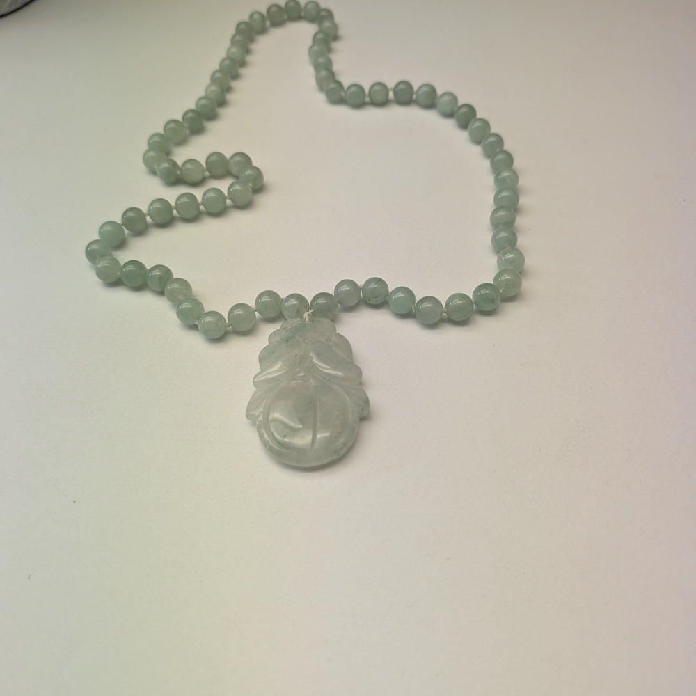 light green jade hand-knotted bead necklace with a carved floral pendant. 